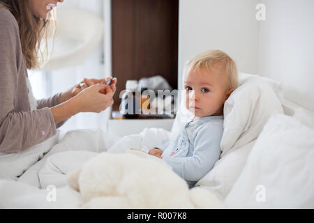 La mère et le bébé en pyjama, tôt le matin, maman prendre soin de son bébé garçon malade. Bébé au lit avec fièvre et écoulement nasal Banque D'Images