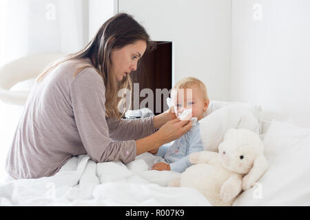 La mère et le bébé en pyjama, tôt le matin, maman prendre soin de son bébé garçon malade. Bébé au lit avec fièvre et écoulement nasal Banque D'Images