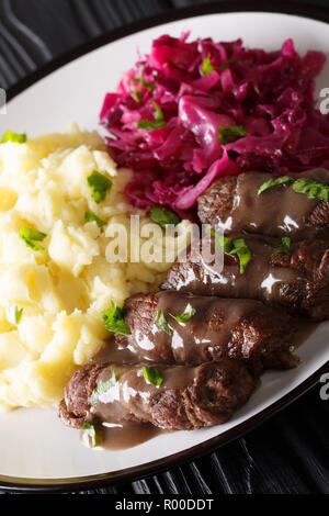 Boeuf Rouladen traditionnel allemand avec une merveilleuse sauce servi avec une purée de pommes de terre et chou rouge gros plan sur une plaque verticale. Banque D'Images