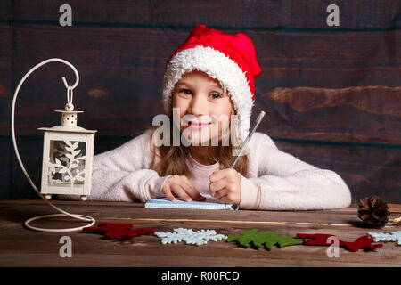 Enfant écrit une lettre au Père Noël . Funny Girl in Santa hat écrit lettre au père à la maison Banque D'Images