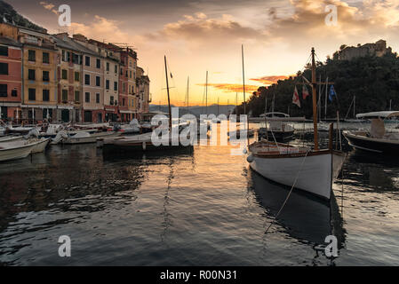 Coucher du soleil sur le port pittoresque de Portofino, sur la Riviera Italienne avec ciel coloré ornage reflétée sur l'eau et la location de voiliers et bateaux de pêche Banque D'Images
