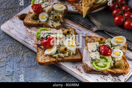 Toasts appétissants de l'avocat, viande, œufs de caille, tomates et fromage bleu Dor. La cuisine de l'auteur. Servant des plats originaux Banque D'Images