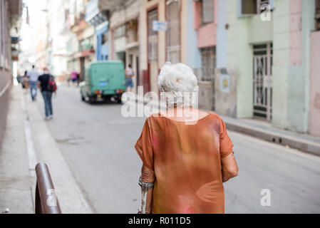 Une vieille femme marche lentement sur le trottoir d'une rue animée de La Havane, Cuba. Banque D'Images