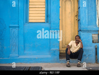 Un homme est assis sur son stoop et regarde le quartier en face d'un immeuble de La Havane colorés. Banque D'Images