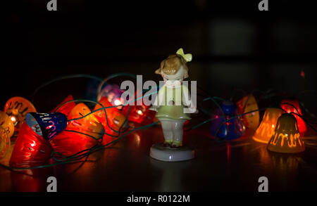 Figurine porcelaine girl avec lumière garland dans l'arrière-plan - Noël sombre intérieur avec des objets vintage européens Banque D'Images