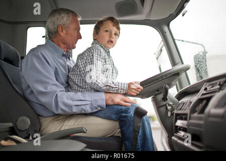 Jeune garçon assis sur les genoux de son père derrière le volant d'un camion. Banque D'Images