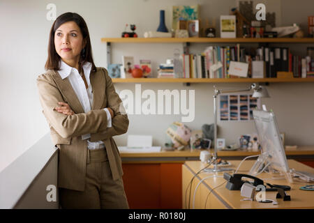 Certain mid-adult businesswoman debout avec les bras croisés tout en regardant par la fenêtre de son bureau. Banque D'Images