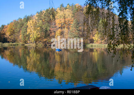 Belle forêt d'automne se reflète dans les eaux calmes d'un lac, avec un pêcheur dans un bleu bateau Banque D'Images