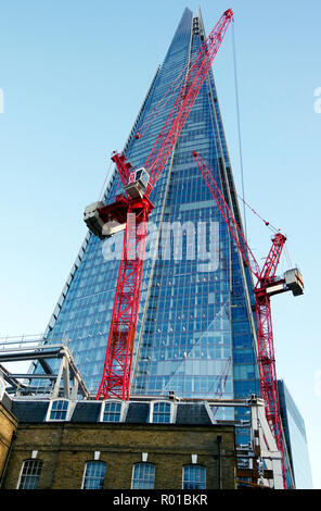 Le Shard, le plus haut bâtiment de la Grande-Bretagne, vue depuis le sol à proximité, avec deux très grandes grues à tour peint en rouge au premier plan. Banque D'Images