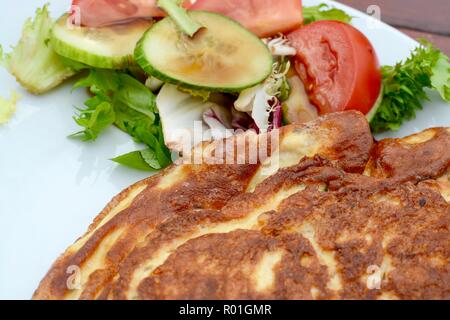 Omelette cuite doré avec salade servi sur une plaque blanche Banque D'Images