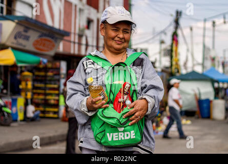 31 octobre 2018, Mexico, Mexico : un disciple de Santa Muerte porte une figure du saint patron dans son sac à dos au lieu de culte dans le quartier de Tepito. Dans sa main elle tient une bouteille avec la liqueur d'agave Mezcal, avec laquelle les statues sont versée au-dessus. Dans la ville de Mexico, des centaines de partisans faisaient des offrandes au saint patron Santa Muerte à l'occasion de la 'Día de los Muertos' ('Day of the Dead'). Les personnes se sont rassemblées le mercredi 31.10.2018 au culte des saints dans le quartier de Tepito. Santa Muerte - en allemand 'holy death' - est représentée par un squelette portant des blouses ou wo Banque D'Images