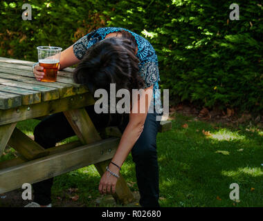 Une femme ivre avec un verre de bière à la main, inconscient, s'appuyant sur une table Banque D'Images