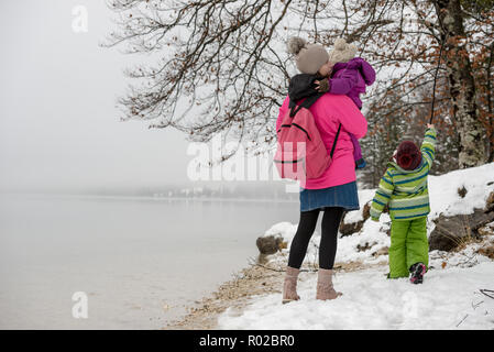 La mère et deux enfants bénéficiant d'une journée d'hiver au bord du lac découvrir la beauté de la nature. Banque D'Images