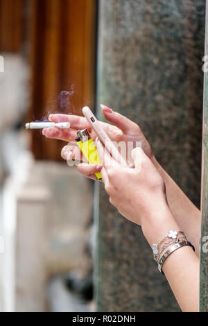 Londres Angleterre,Royaume-Uni,Mayfair,cigarette,fumer de la fumée,trottoir extérieur,mains de femme,utilisation de smartphone,addiction à la nicotine,tenir un briquet,vérifier regarder Banque D'Images