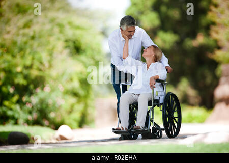 Man poussant sa femme dans un fauteuil roulant. Banque D'Images