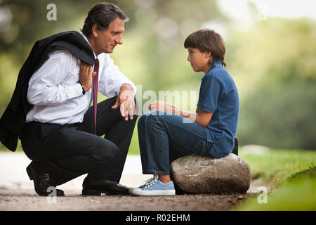 L'homme accroupi à côté de l'entreprise à son fils sur le trottoir. Banque D'Images