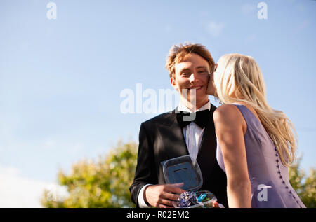 Teenage boy holding corsage en conteneur que sa date de bal d'embrasse sa joue. Banque D'Images