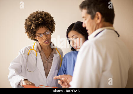 Trois médecins de discuter des dossiers de patient dans un couloir. Banque D'Images