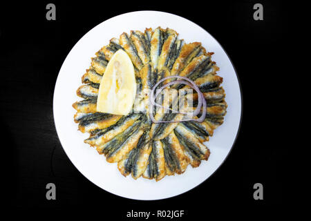 Anchois frits turc (hamsi tava), les citrons et l'oignon sont servis avec plaque blanche en arrière-plan noir. Banque D'Images