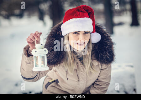 Beautiful Girl in Santa hat sur forêt d'hiver avec Noël lanterne Banque D'Images