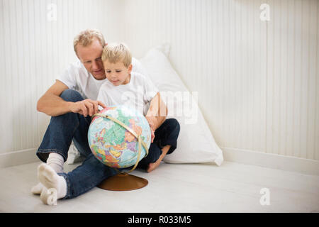 Mid-adult man sitting avec son jeune fils à la recherche d'un globe. Banque D'Images