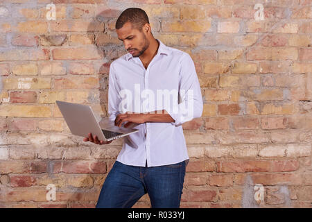 Un beau jeune homme à l'aide d'un ordinateur portable dans une chemise blanche. Banque D'Images