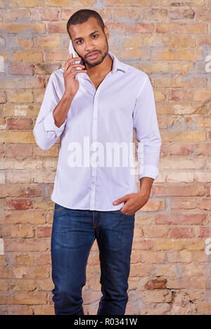 Un beau jeune homme en conversation sur son téléphone dans une chemise blanche. Banque D'Images