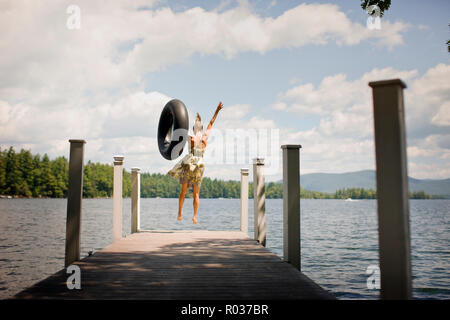 Femme avec tube intérieur, sautant hors d'une jetée dans un lac. Banque D'Images