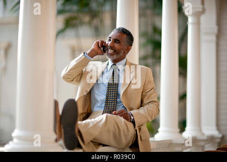 Mature businessman sitting par des piliers en face de son hôtel et de parler sur son téléphone cellulaire. Banque D'Images