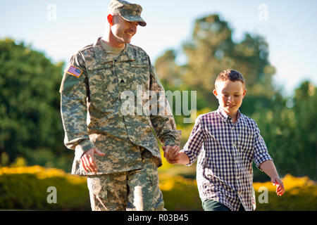 Soldat de l'armée se tenant la main avec son jeune fils dans leur cour arrière. Banque D'Images