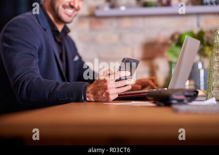 Un beau jeune homme d'affaires heureux en utilisant son smartphone en environnement de bureau. Banque D'Images