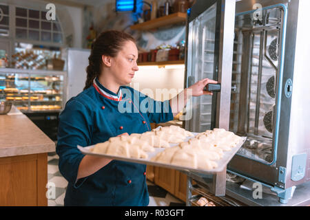Boulanger français portant veste bleue mettant croissants au four Banque D'Images