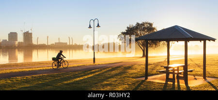 Une personne à vélo par Sir James Mitchell Park au lever du soleil sur un misty et crisp journée d'hiver. South Perth, Australie occidentale Banque D'Images