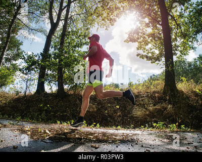 Coureur de l'homme pantalon short noir jaune et rouge t-shirt saute sur la piscine sur route asphaltée. Soirée fitnes exercice dans le parc automne Banque D'Images