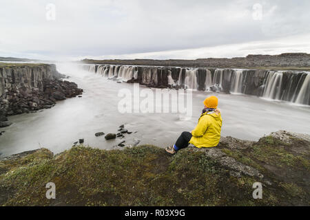 Femme en imperméable jaune assis debout sur le bord de la falaise à côté de Selfoss waterfall dans Vatnayokull, parc national de l'Islande. Banque D'Images