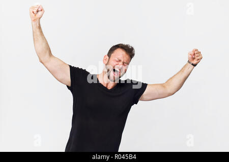 Beau jeune homme avec le beau sourire de victoire posant des gestes contre fond blanc Banque D'Images