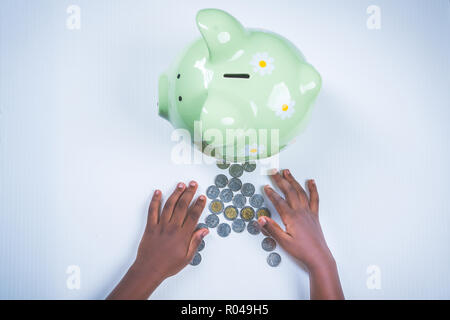 Fille noire à compter des pièces par piggy bank Banque D'Images