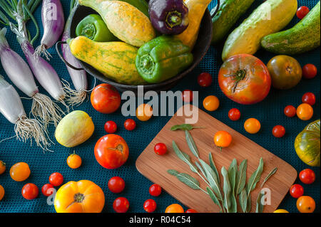 Une abondance de produits frais, y compris les oignons, la tomate, la courge, le poivre, la sauge et le concombre sur un fond de couleur bleu sarcelle. Banque D'Images