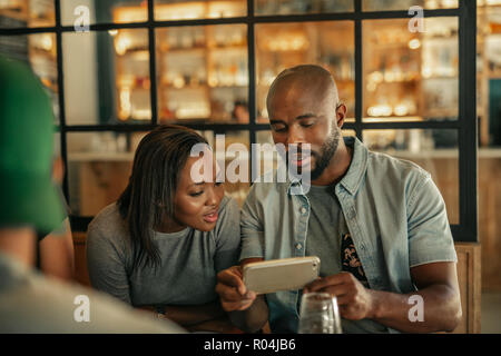 Deux amis assis dans un bar à la recherche de photos de cellulaire Banque D'Images