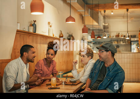 Smiling friends parle plus de boissons et nourriture dans un bistro Banque D'Images