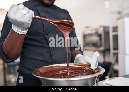 Le chocolat fondu en remuant travailleur dans un bol en acier inoxydable Banque D'Images