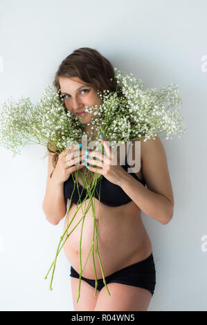 Femme enceinte avec bouquet de fleurs dans les mains , mur blanc sur fond Banque D'Images