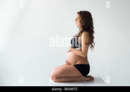 Séance femme enceinte avec les mains sur le ventre, sur fond de mur blanc Banque D'Images