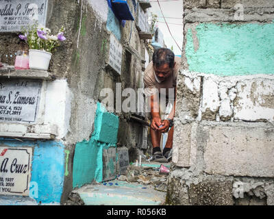 Manille, Philippines. 1er novembre 2018. Un homme presser son corps pour s'adapter à des piles de type appartement à tombes allumer une bougie pour son parent décédé.Des millions de Philippins troupeau aux cimetières à travers le pays pour rendre visite à leurs défunts amoureux. Payer leurs respects à des êtres chers qui sont morts. C'est la tradition et la culture philippine. Credit : Josefiel Rivera SOPA/Images/ZUMA/Alamy Fil Live News Banque D'Images