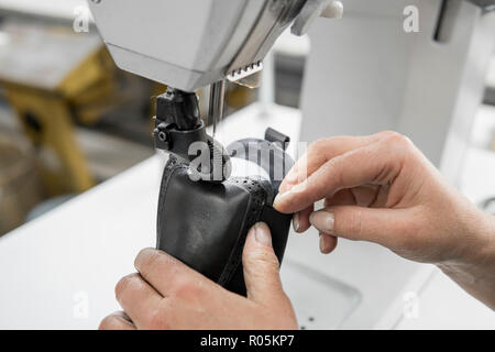 Machine à coudre dans un atelier de cuir en action avec les mains sur un travail pour des détails en cuir chaussures. Old Women's Hands avec machine à coudre à la fabrique de chaussures. Banque D'Images