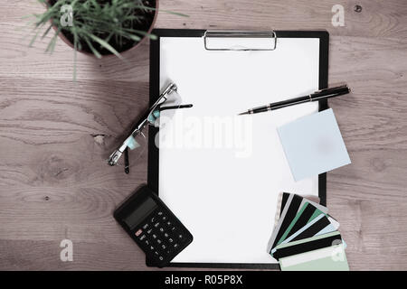 Vue de dessus.Presse-papiers avec une feuille blanche, un stylo, lunettes et calculatrice Banque D'Images