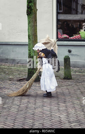 Deventer, Pays-Bas, le 21 décembre 2014 : Petite fille en robe costume victorien balaie la rue avec un balai pendant le festival Dickens dans de Banque D'Images