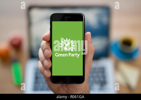 Un homme se penche sur son iPhone qui affiche le logo du Parti Vert, tout en s'assit à son bureau informatique (usage éditorial uniquement). Banque D'Images