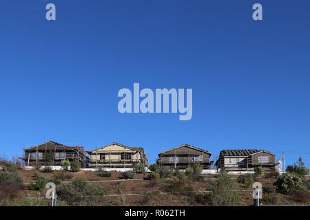 Quatre nouvelles maisons en construction d'échafaudages, sur une petite colline, certains arbustes, un mur. Grande quantité de ciel bleu au-dessus d'eux pour obtenir une copie de l'espace. Banque D'Images