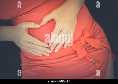 Pregnant belly closeup, mains formant le cœur, robe rouge, belle photo Banque D'Images